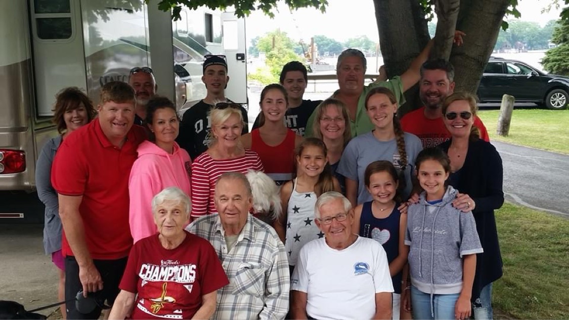 Three generations of family gathered at West Harbor Club beside a motorhome, with the harbor behind them